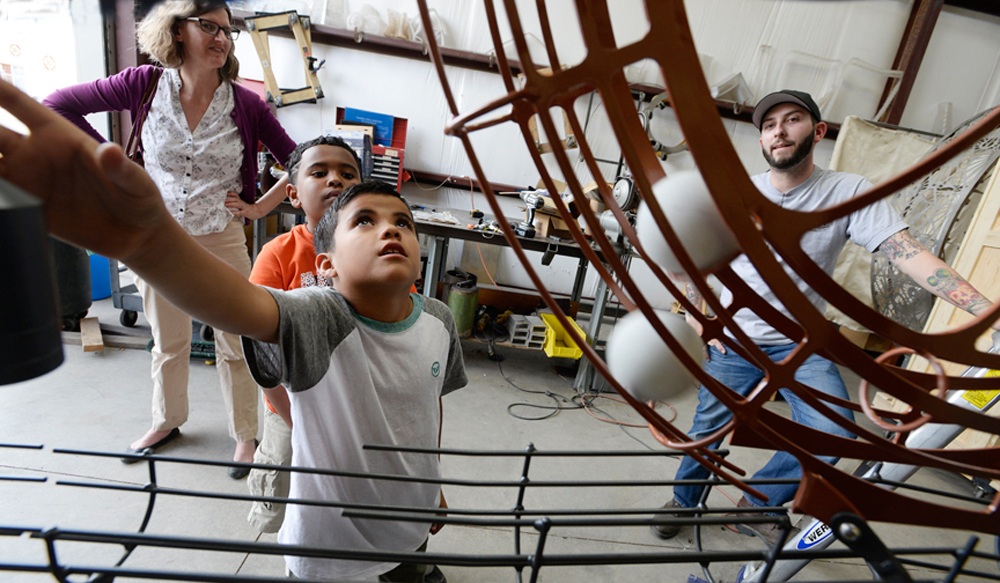 Student, community partner, educator at Creative Machines. Student points up at machine in wonder.