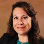 Photo of Advisory Board member Nicole Allard, smiling in blazer with teal shirt and brunt orange background