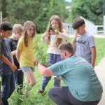 Students observe plants in pots alongside their teacher